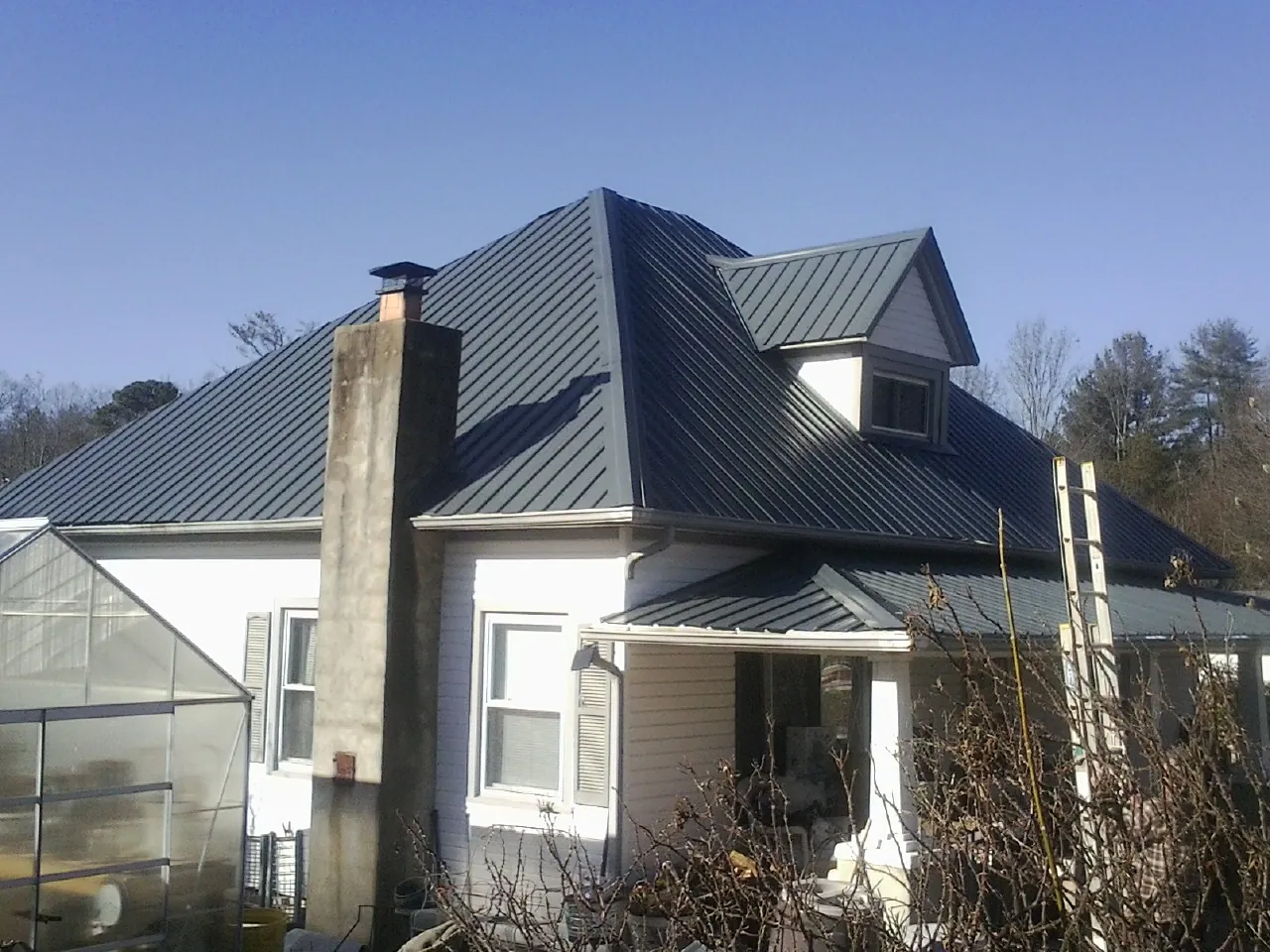 Dark blue standing seam metal roof on a white farmhouse with dormer — Slate & Tile Roof Repair by Roofing Brothers in Brandamore