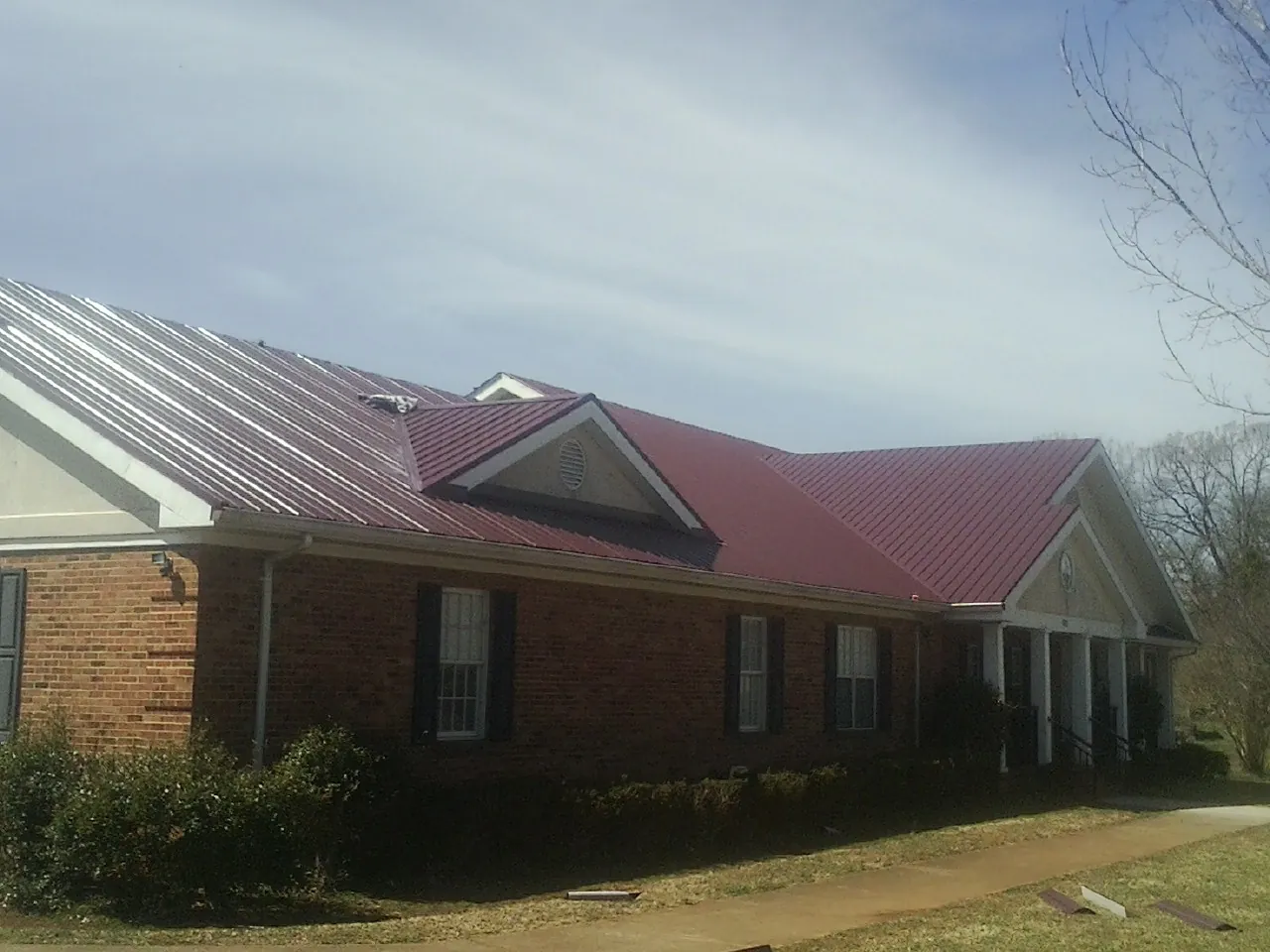 Red metal roof with gabled entries on a long brick building, from a Hail Damage Roof Repair job in Brandamore