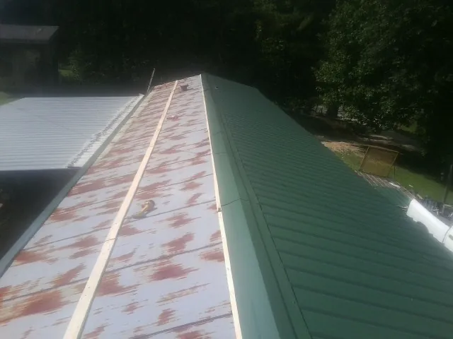 Old rusted panels beside newly installed green metal roofing — Wind Damage Roof Repair by Roofing Brothers in Brandamore
