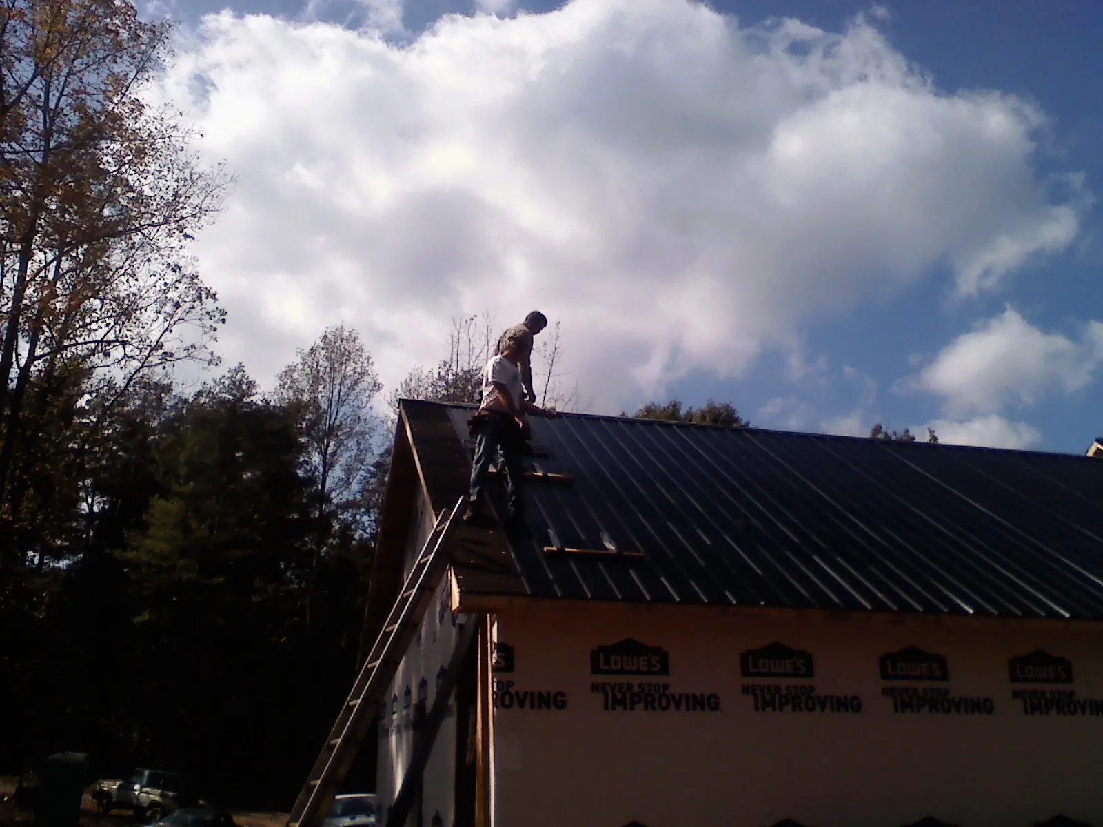 Roofer fastening dark metal panels high against a cloudy sky, from a Roof Inspection job in Brandamore