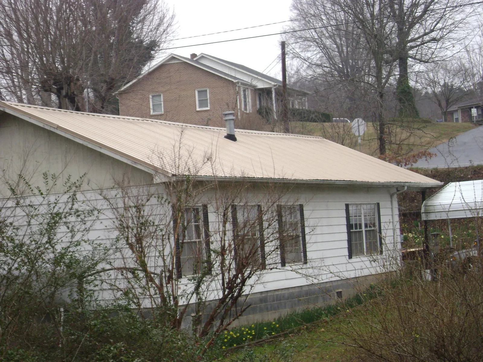 Tan metal roof on a white sided house set into a hillside — Commercial Roofing by Roofing Brothers in Brandamore