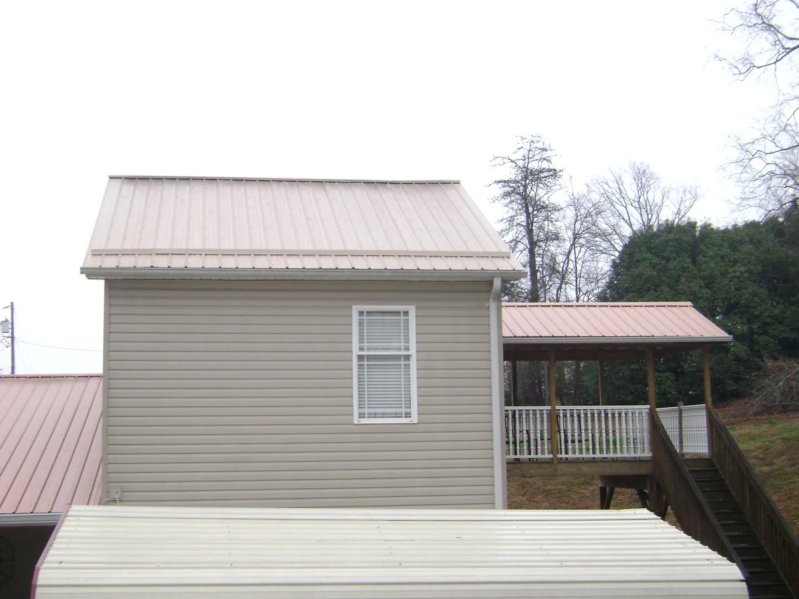 Tan metal roofs on a two story addition and attached porch, from a Roof Replacement job in Brandamore